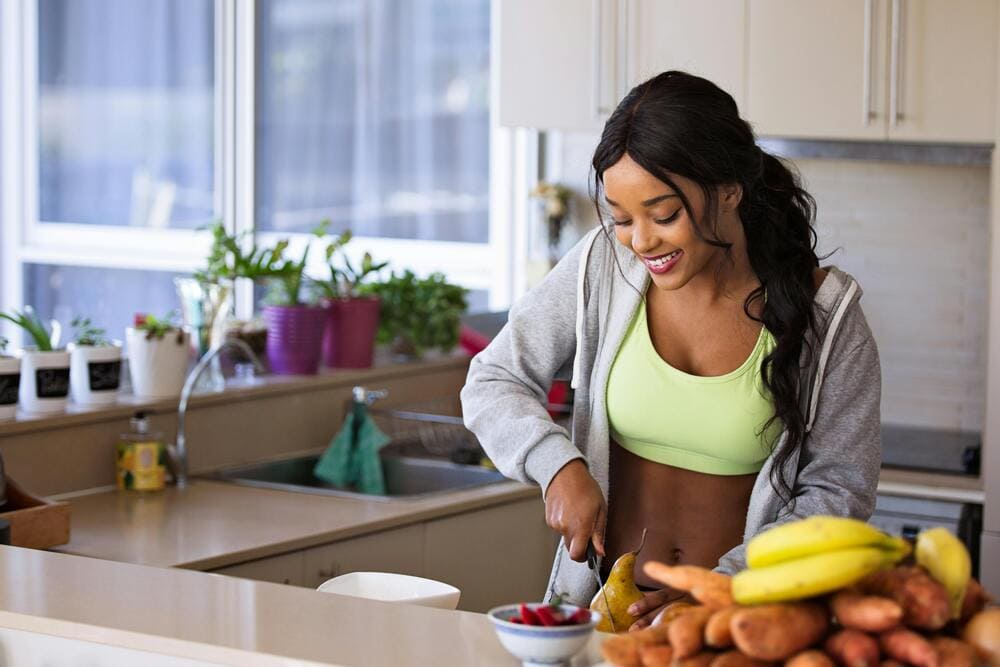 jeune femme souriante en train de préparer une salade de fruits dans sa cuisine 