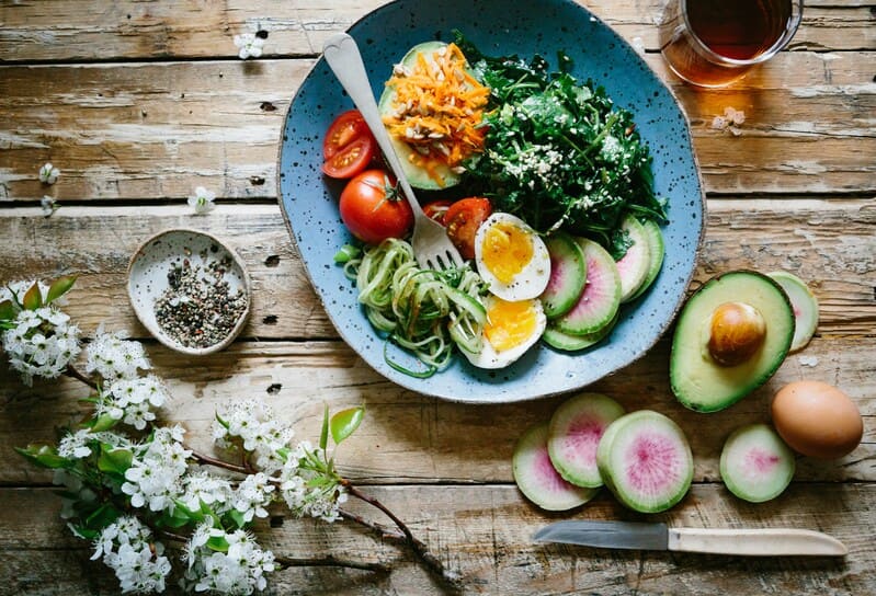 assiette santé contenant des légumes, de l'oeuf, de l'avocat sur une table en bois brut 